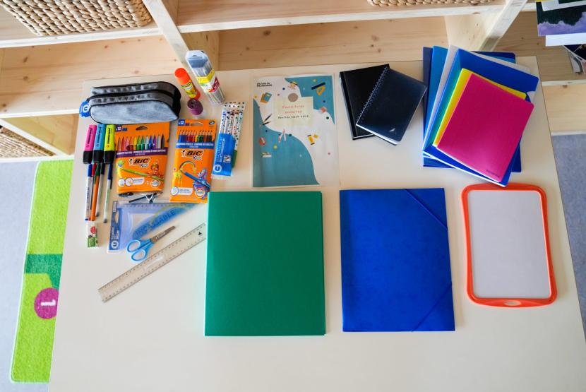 Table avec des cahiers, classeurs, crayons qui composent le kit scolaire.