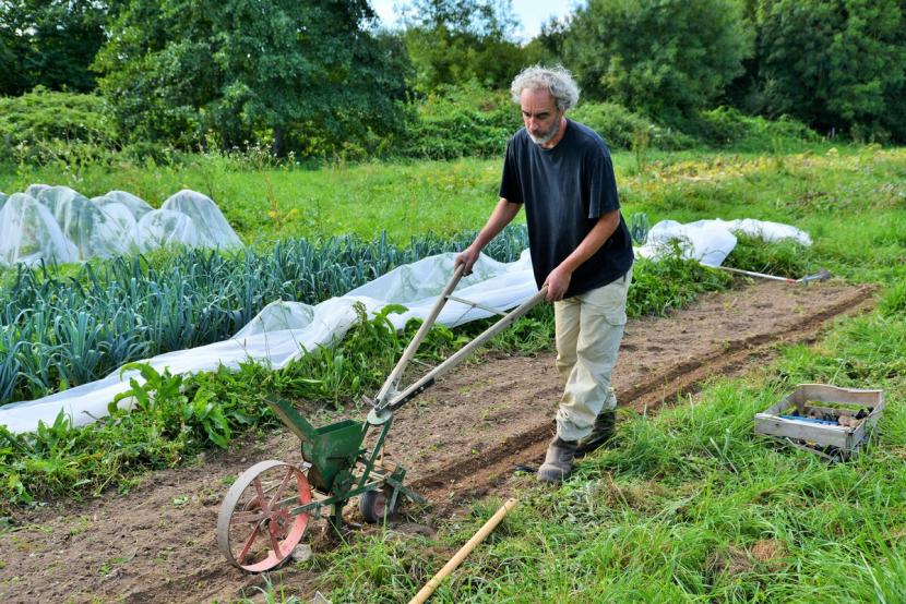 un homme retourne de la terre avec un outil